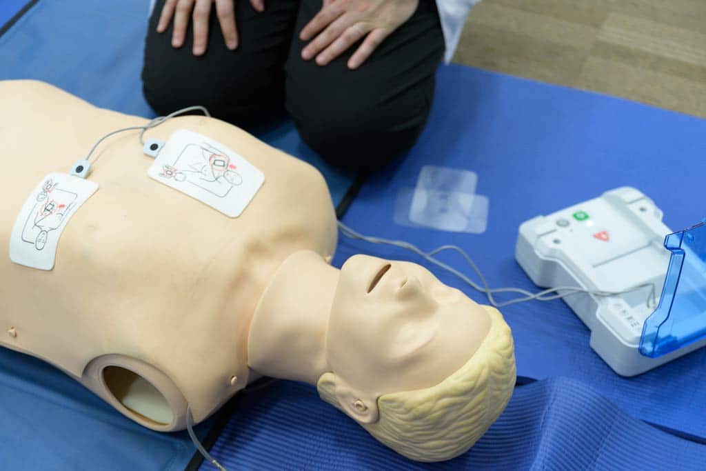 Person kneeling beside a dummy with AED pads attached